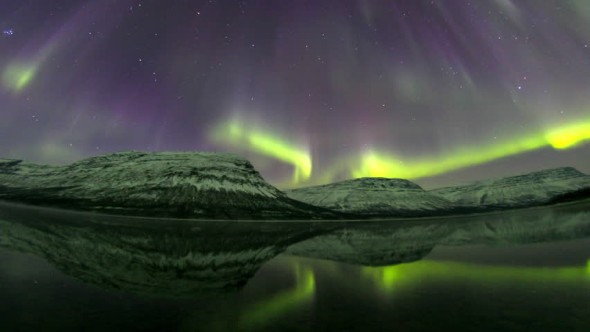 Astonishing aurora borealis lighting the starry sky above a calm lake with mountain reflections