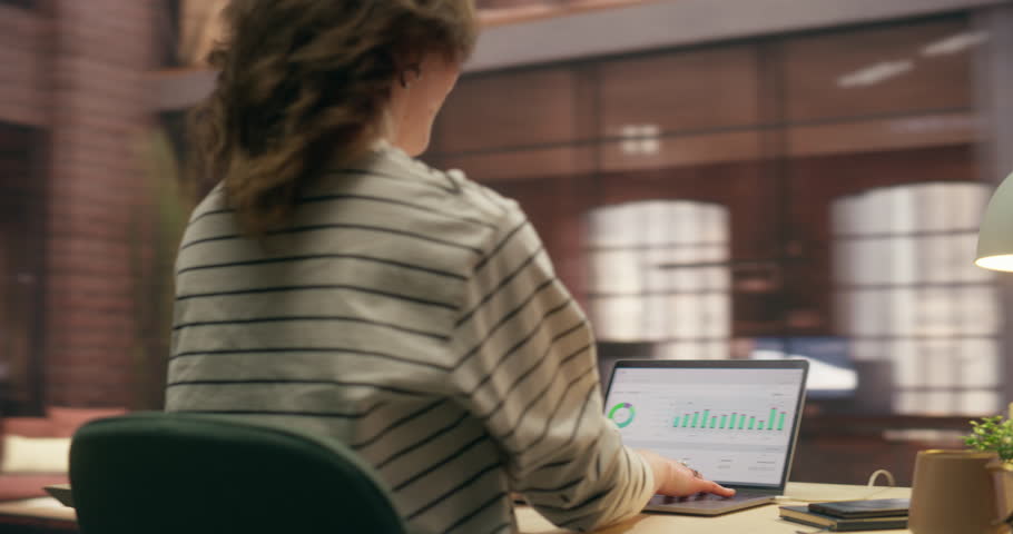 360 Degree. Caucasian Woman Celebrates Success at Office Desk, Then Analyzes Ecommerce Data on Laptop, Tracking Online Growth and Digital Business Profit Achievement. Cinematic Arc Tracking Shot.