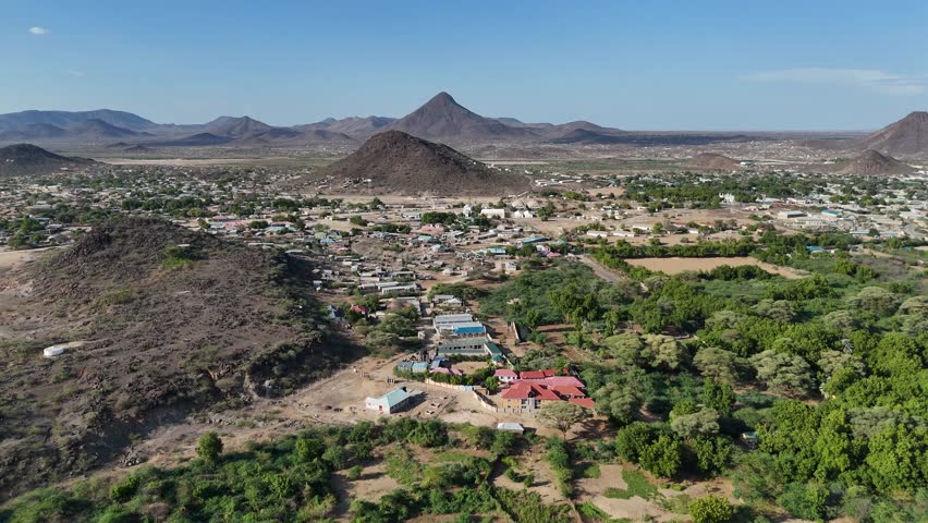 Aerial view of Lodwar, Turkana County, Kenya, with green river-side vegetation, town buildings, and rocky hills under a clear sky.