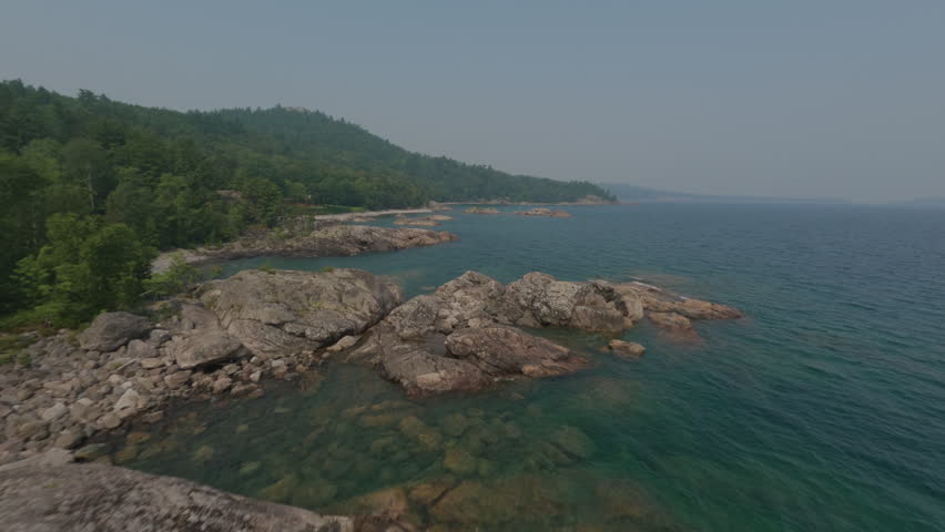 Beautiful aerial perspective of a remote, rocky shoreline with a lush green forest meeting the clear water of Lake Superior