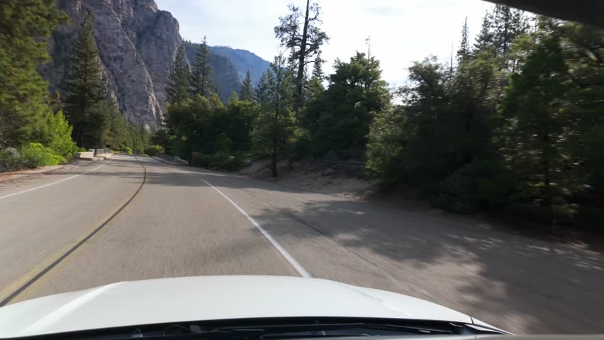Vehicle-mounted footage travels along a winding roadway through Kings Canyon National Park, passing towering granite cliffs, pine forests, and dramatic Sierra Nevada scenery in California.