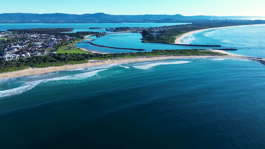 Drone aerial landscape of ocean waves crashing onto the shoreline at Warilla Beach with Windang Passage and Lake Illawarra in the background Wollongong South Coast NSW Australia tourism and travel