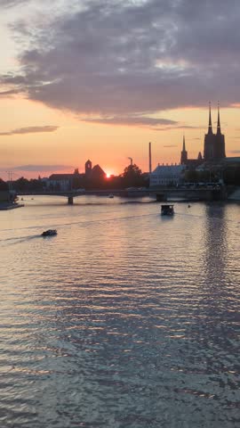 Tourist boat cruising on Oder River at sunset with Ostrow Tumski cathedral skyline silhouette in Wroclaw, Poland. Scenic golden hour European city travel cruise destination and vacation concept.