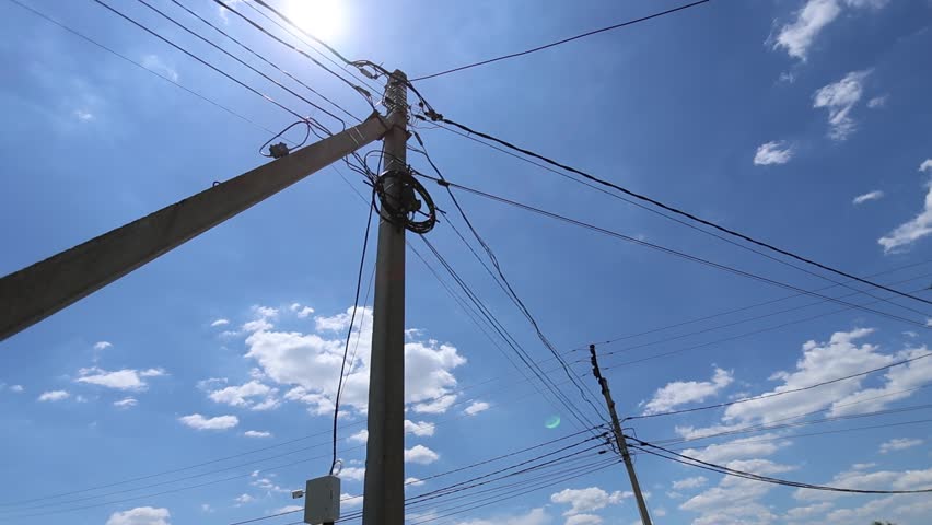 Low angle view of utility poles and overhead power lines crossing sunny blue sky