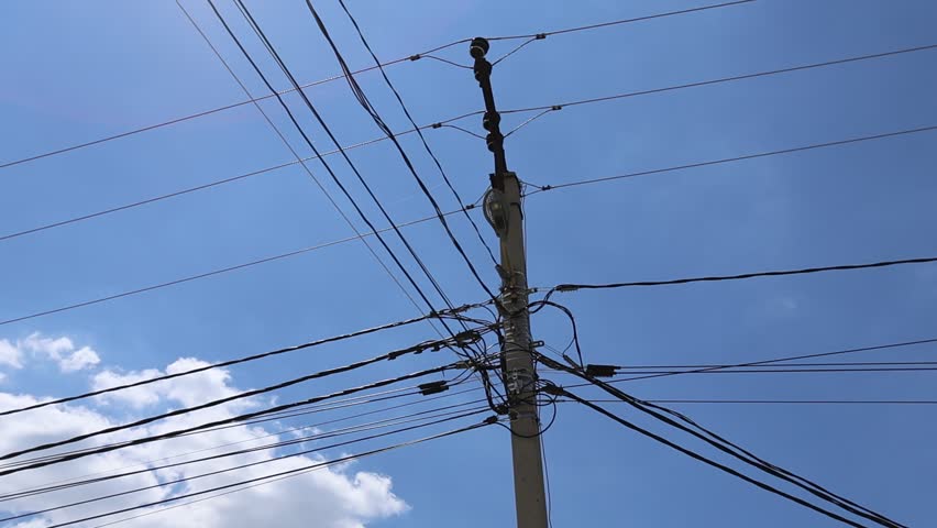 Utility pole with dense overhead power cables against blue sky in urban daylight scene