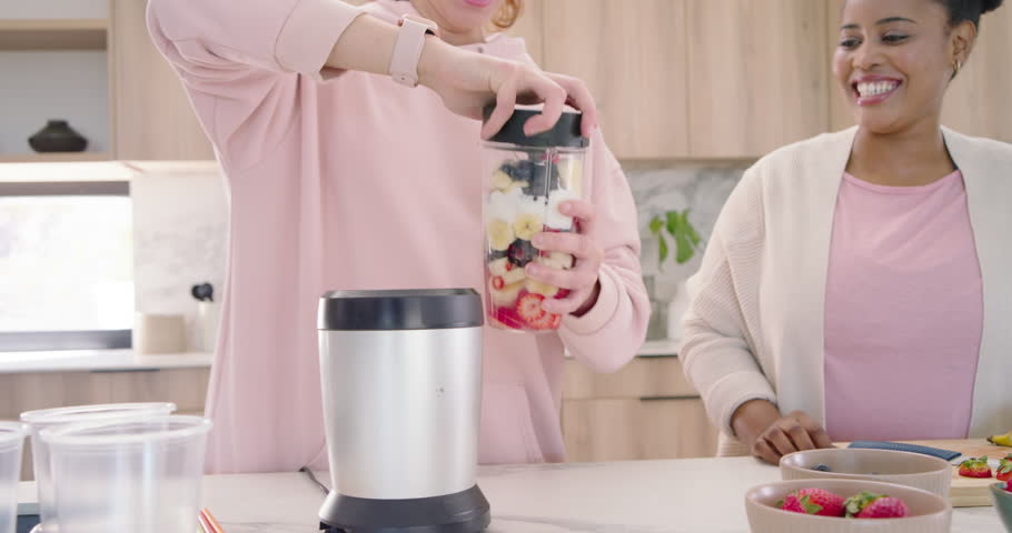 Diverse female friends with center woman securing blending cup on blender base, making smoothie. Kitchen, island, bright, vibrant, fruit, yogurt, strawberries