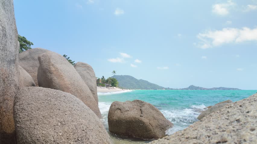 Waves gently washing over large granite boulders on a tropical beach shoreline
