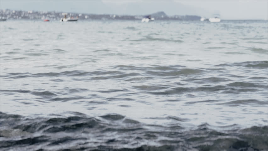 Calm lake waves rolling towards a rocky shoreline under an overcast grey sky