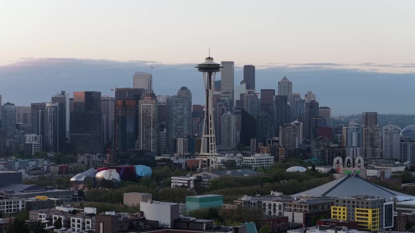 Seattle skyline glows at dusk with Space Needle rising above downtown skyscrapers, colorful MoPOP museum, stadium and Elliott Bay waterfront in Seattle, Washington, USA. Aerial drone wide shot