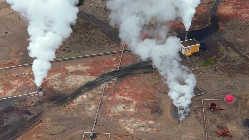 Aerial perspective of the Bjarnarflag geothermal power station in Iceland. White steam billows from vents in a colorful volcanic area