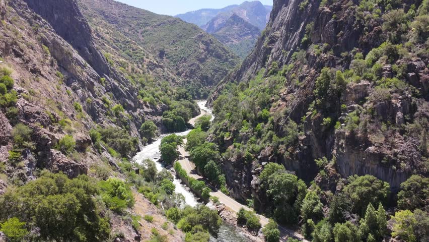 Aerial drone footage follows the Kings River as it winds through a dramatic granite canyon surrounded by steep cliffs, rugged terrain, and lush vegetation near Kings Canyon National Park, California.