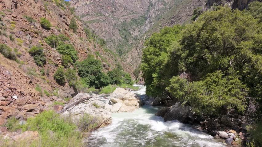 Aerial drone footage glides above rushing whitewater rapids on the Kings River, weaving through granite boulders and steep canyon walls surrounded by rugged vegetation near Kings Canyon National Park