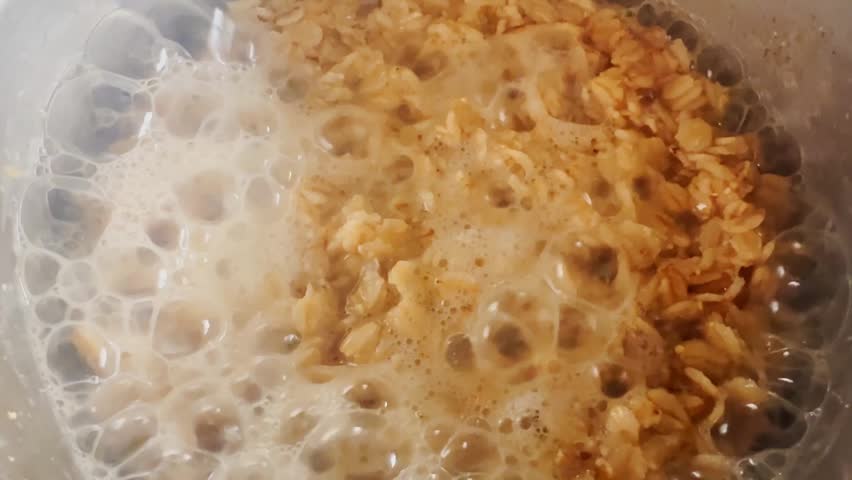 Close-up of oats boiling with bubbling foam in a pot, showing warm porridge texture and simple homemade breakfast preparation.