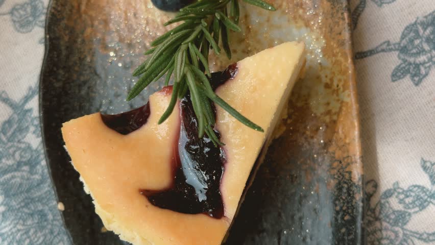 Indulge in a rich, creamy blueberry cheesecake slice, beautifully presented with rosemary, perfect for a delightful cafe experience.