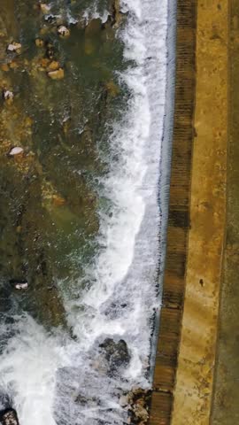 Vertical drone view of the Sava River weir in Tacen, Ljubljana, with white water flowing over the dam beside rocky green water.