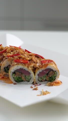 Spicy tuna sushi roll with crispy onion and chili topping spinning on a white plate, isolated on a white background
