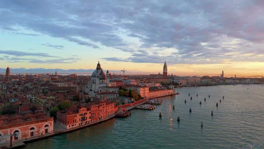 Venice aerial sunset over lagoon, boats gliding past basilica santa maria della salute, pastel sky casting. Italy