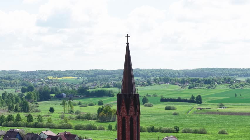 Aerial drone footage capturing iconic gothic church steeple silhouette standing tall above scenic green countryside with distant hills and rolling fields under expansive summer sky.