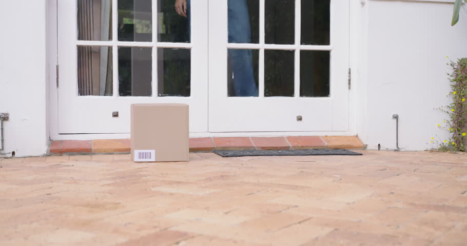 Woman in yellow top spotting package stepping out to retrieve parcel, checking barcode closing door. Box, doormat, porch, entryway, delivery, candid, homeowner