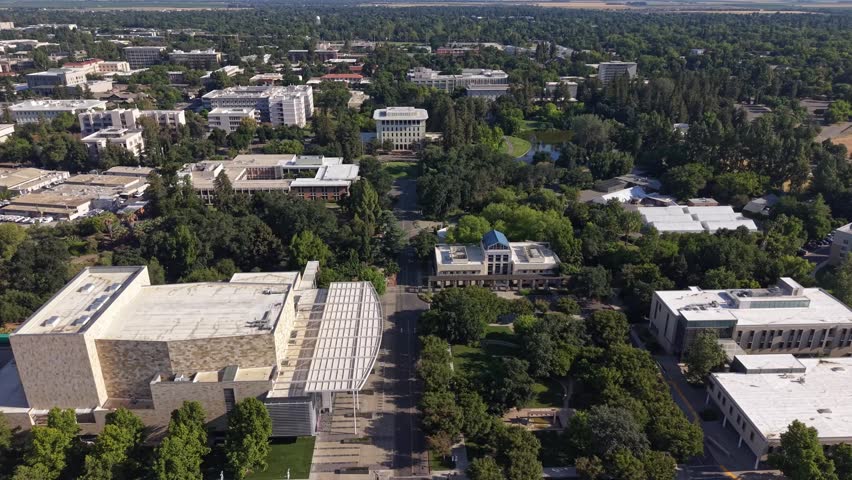 Aerial view capturing sprawling university campus featuring modern academic architecture surrounded by mature trees lush landscaping and walking paths during bright sunny day outdoor footage.
