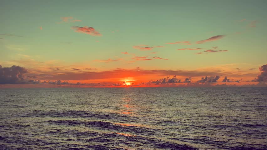 Sunset glowing over the calm ocean with colorful clouds in the sky creating a tranquil seascape view