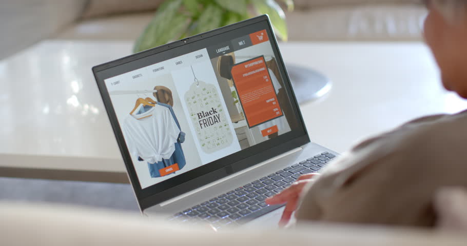 African woman browsing laptop at home, seeing Black Friday tag, scrolling orange menu, copy space. Computer, ecommerce, scrolling, shopping, couch, plant, lamp