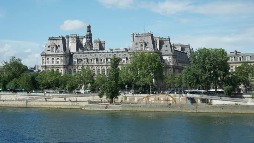 Hotel de Ville city hall building stands by Seine river in Paris France. European architecture landmark view with heritage facade and green trees during summer tourism travel destination trip.