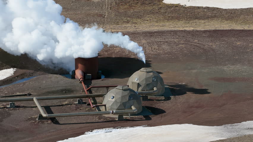 Steam emanates from volcanic site. Vast geothermal installation amid volcanic and mountain scenery