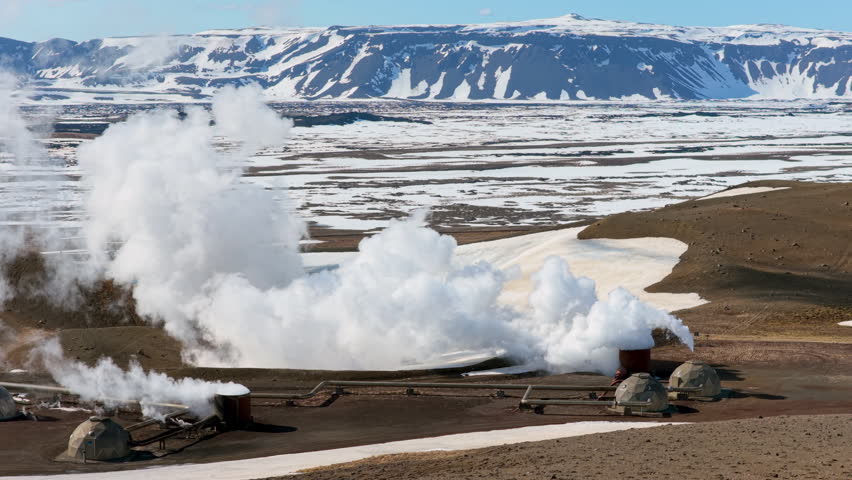 Steam emanates from volcanic site. Vast geothermal installation amid volcanic and mountain scenery