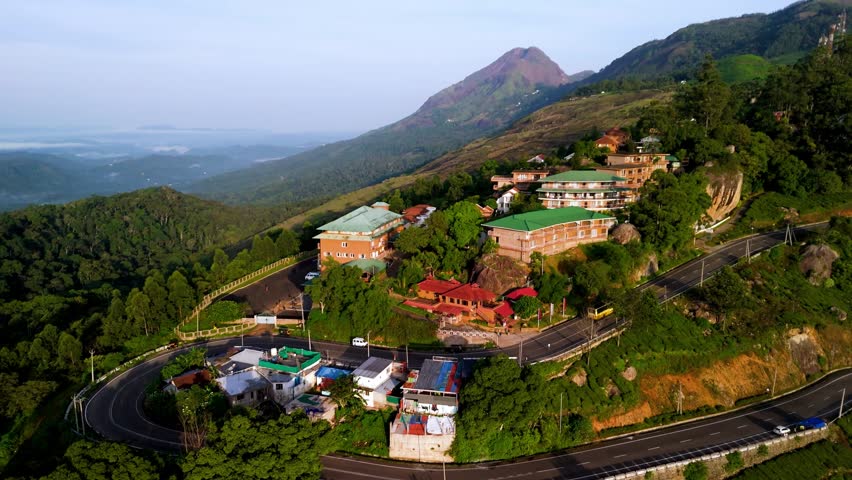 Scenic Aerial View of U Turn Mountain Road Passing Through Green Hills with Small Houses in Center, Surrounded by Mountain Landscape, Rural Settlement, Lush Nature and Beautiful Countryside Scenery