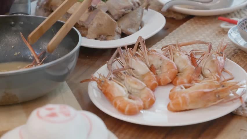 Family hands serving large cooked river prawns or giant tiger shrimps on a white plate during a traditional dinner.