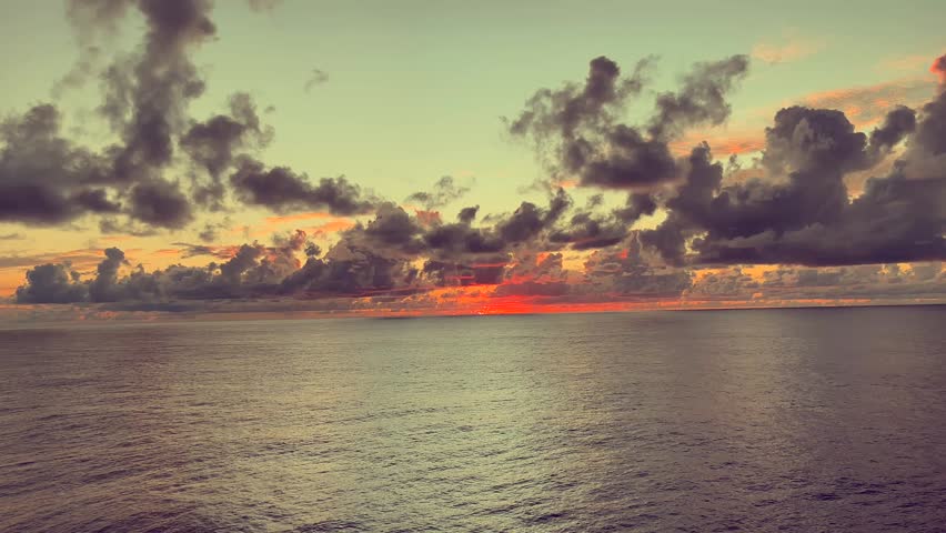 Dramatic sunset over calm ocean with colorful clouds and reflections on tranquil water