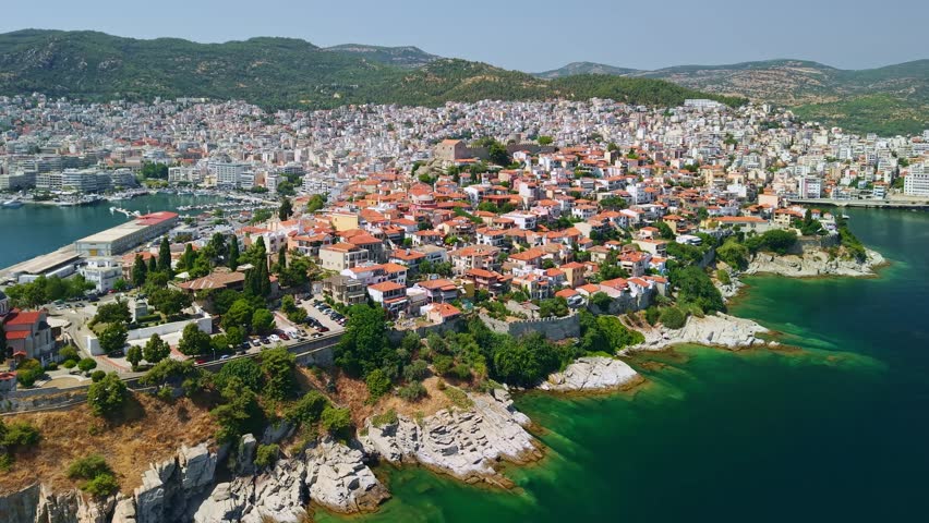 Aerial view of the historic Panagia district in Kavala, Greece. The medieval fortress crowns the hilltop above traditional red-tiled houses, the Imaret complex, and the Aegean Sea coastline.