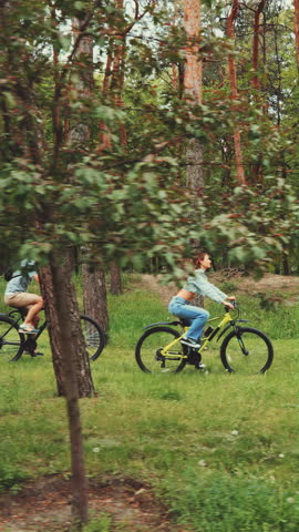 Man and woman cycling through lush green forest on a warm day, enjoying nature, active lifestyle, and peaceful outdoor time together.