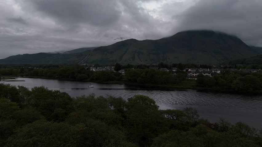 Aerial drone push forward shot of Ben Nevis in Scotland. Shot from the town Fort Wiliam over a lake with surrounding trees at night.