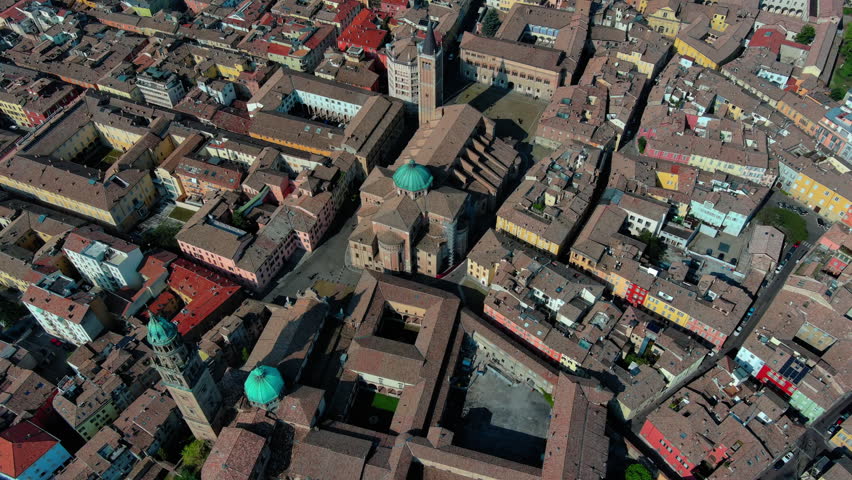 Top-down drone view of Parma Cathedral, Baptistery, and Piazza Duomo amid terracotta rooftops in Parma, Emilia-Romagna, Italy, daytime.