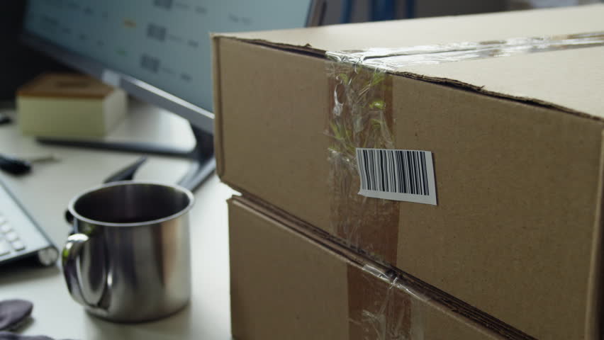Cropped shot of warehouse worker scanning barcode on cardboard box using handheld laser scanner and reaching for metal mug. Footage is perfect for e-commerce, logistics, and shipping commercials
