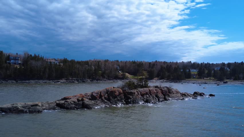 Scenic aerial capture of one of Canada’s oldest reinforced concrete lighthouses beside the vast St. Lawrence River.