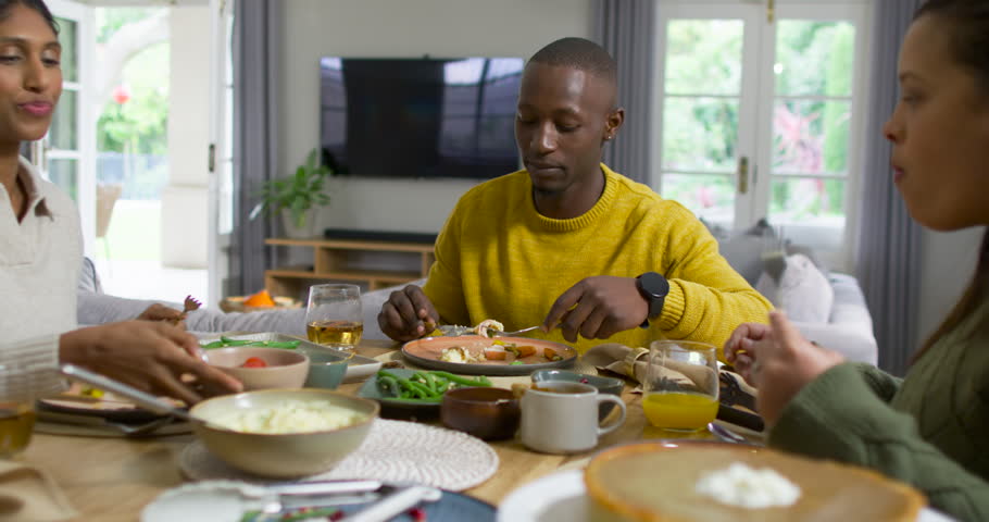 Family dining at table, African man in yellow sweater picking up fork, serving rice, talking. Meal, lifestyle, cozy, stock, home, outdoors, plant