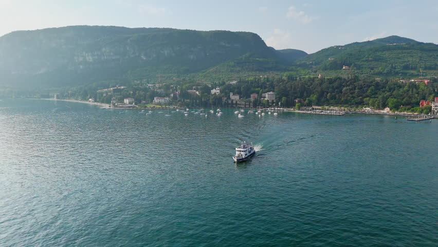 Ferry crossing Lake Garda with distant urban area and marina, connection between lakeside locations