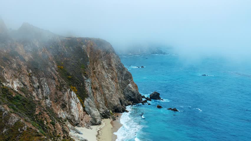 Big Sur. Aerial view of coastal landscape with cliffs and misty sea, featuring a sandy beach and rocky coastline.