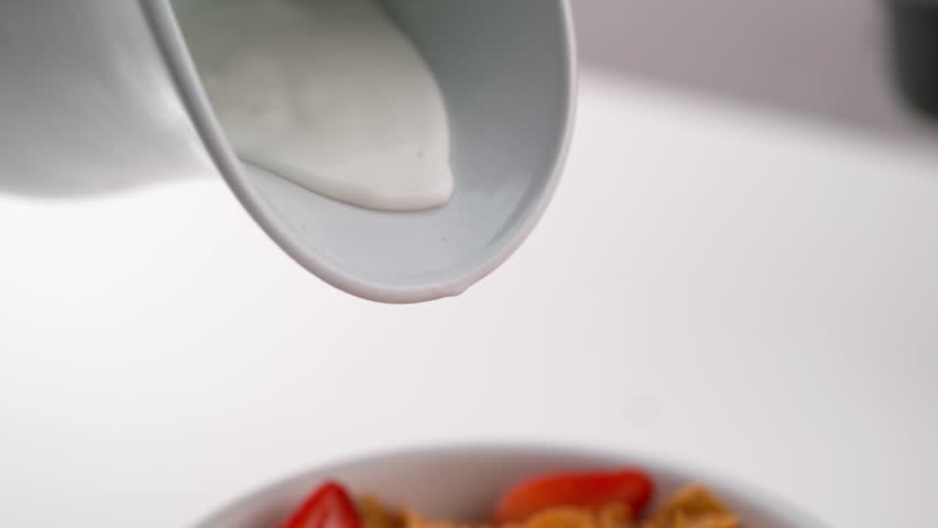 Pouring Milk onto Cereal with Strawberries. Slow motion video of milk being poured over cereal and strawberries in a bowl.