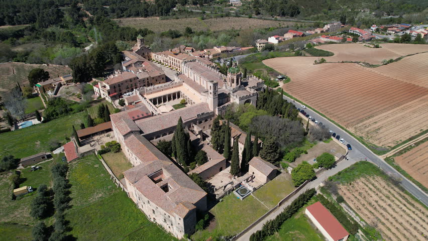 Backward reveal aerial shot of Santa Maria de Poblet Monastery on sunny spring day. Tarragona Province, Spain.