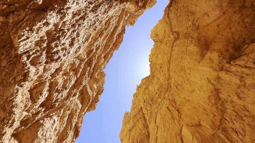 POV Tilt Up From Narrow Gorge to Red Rock Spires in Bryce Canyon National Park. A smooth low angle cinematic shot looking up from a narrow canyon gorge at unique red sandstone spires in Bryce Canyon, Utah. Majestic otherworldly shapes against a clear blue sky. USA.