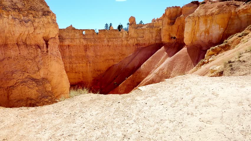 ⛰️ Bryce Canyon Depth: POV From Canyon Floor Looking Up. A smooth first-person POV video from the canyon floor, looking up at towering red sandstone cliffs and hoodoos with green pine trees on top. Beautiful clear blue sky on a sunny day. Wilderness.