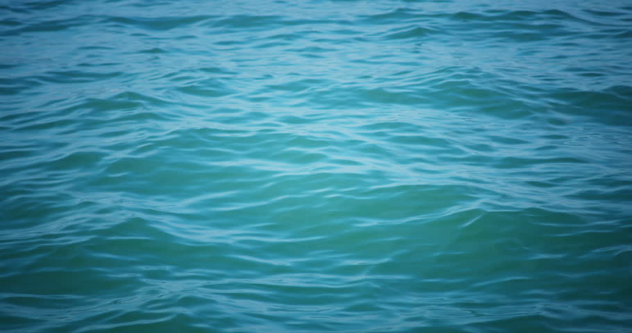 Close up of turquoise ocean waves moving gently under sunlight. Cinematic deep blue sea water surface background.