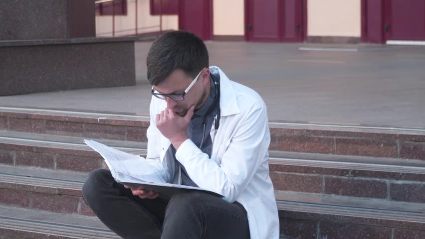 Concept of education, science, health and medicine. Medical students sitting on stairs outside building studying, doing homework, preparing for exams and tests. Student sitting outside on campus
