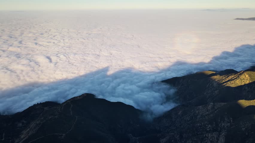 Aerial shot of mountains rising above a layer of low clouds at sunrise. Southern California.