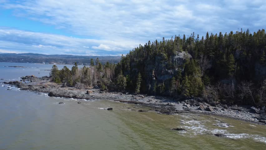 Aerial view of Quebec’s rugged coastline featuring forested shores, rocky outcrops, and rolling waves along the St. Lawrence River.