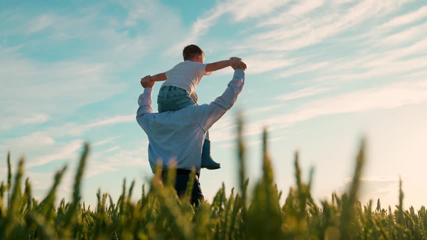 Kid son father play, enjoy nature outdoor, dream of flying, super hero. Family, dad kid with child on their shoulders run through wheat field. Child dreams of fly. Dad, boy child walk together, sky